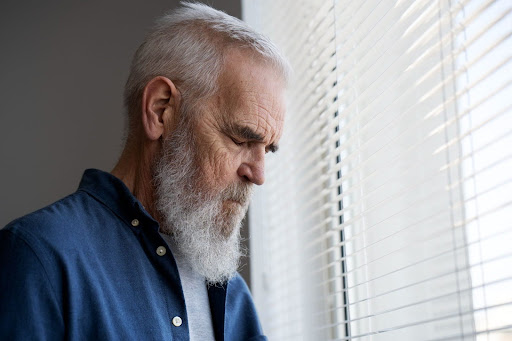 Old man standing alongside window