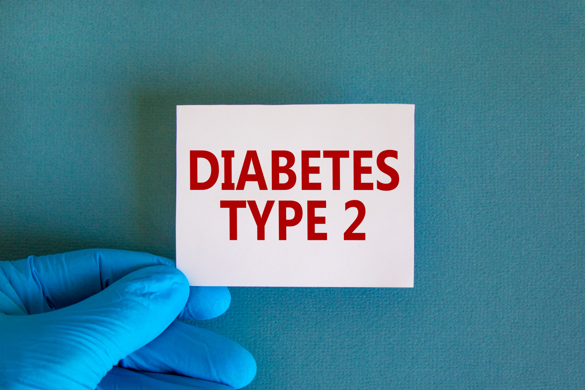 Gloved hand holding a card that reads ‘Diabetes Type 2’ against a teal background