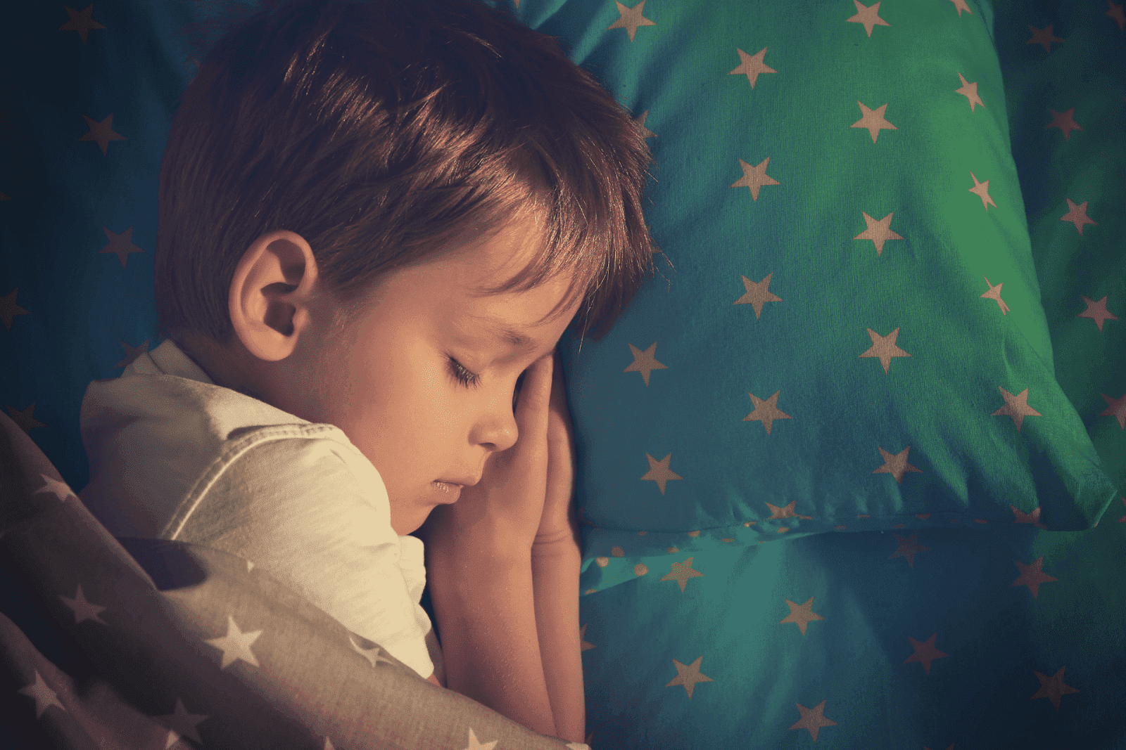 A child is asleep, lying on a green pillow with star patterns and covered with a matching blanket