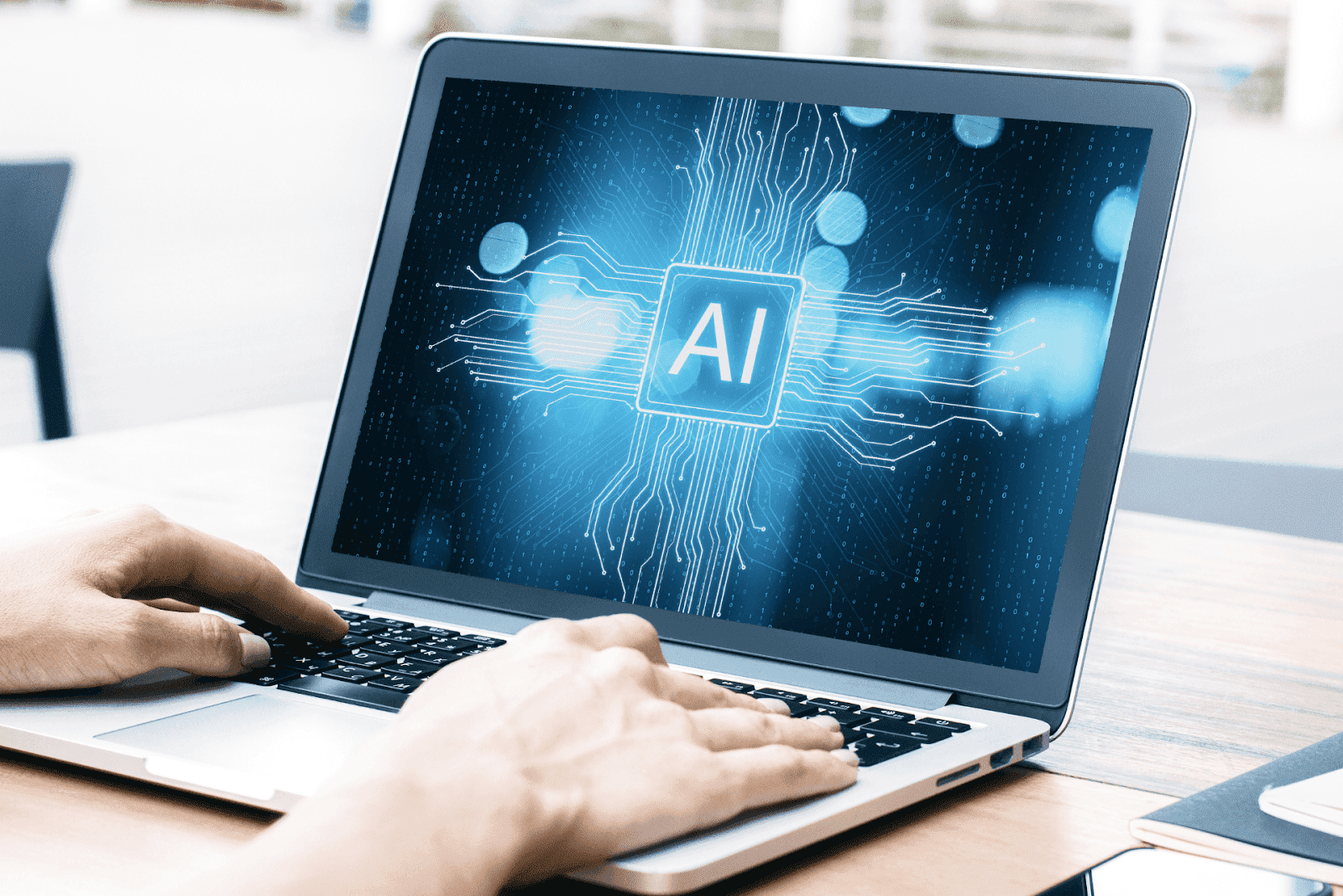A close-up of hands typing on a laptop that displays a glowing “AI” icon at the center of the screen