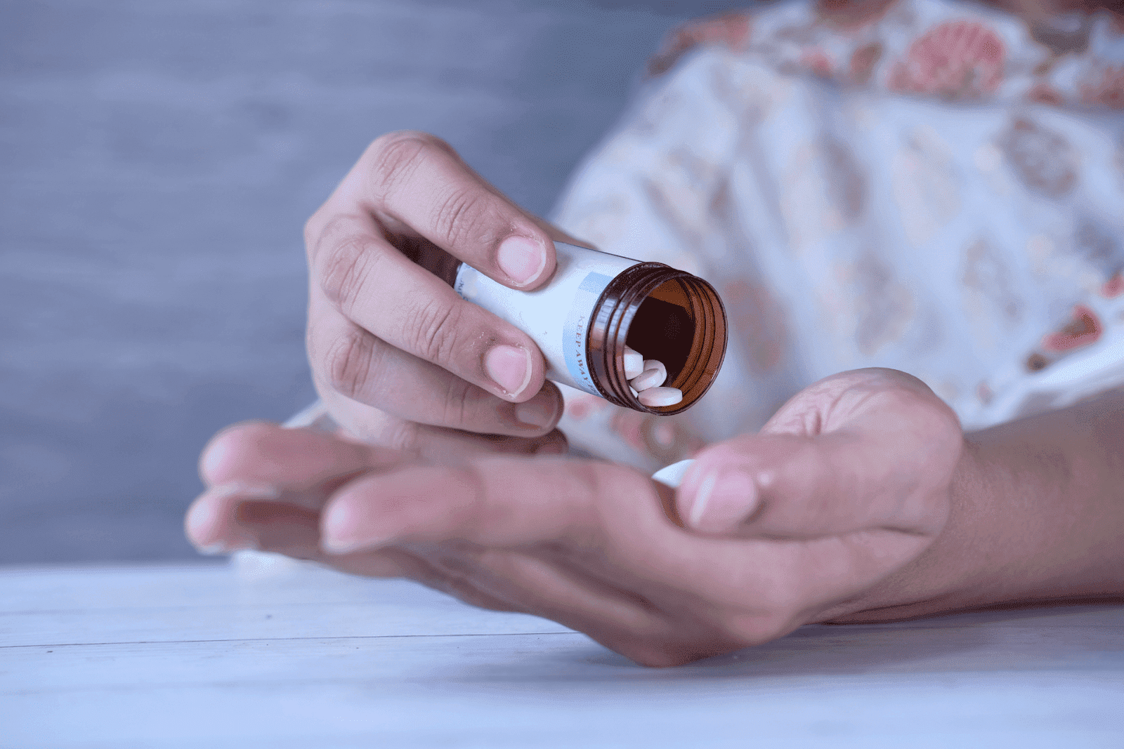 A hand pouring small white pills from a brown bottle into the palm..