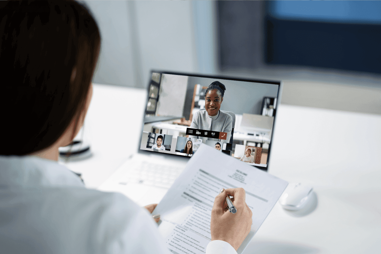 A healthcare provider on a video conference, reviewing a document while speaking with multiple people on screen.