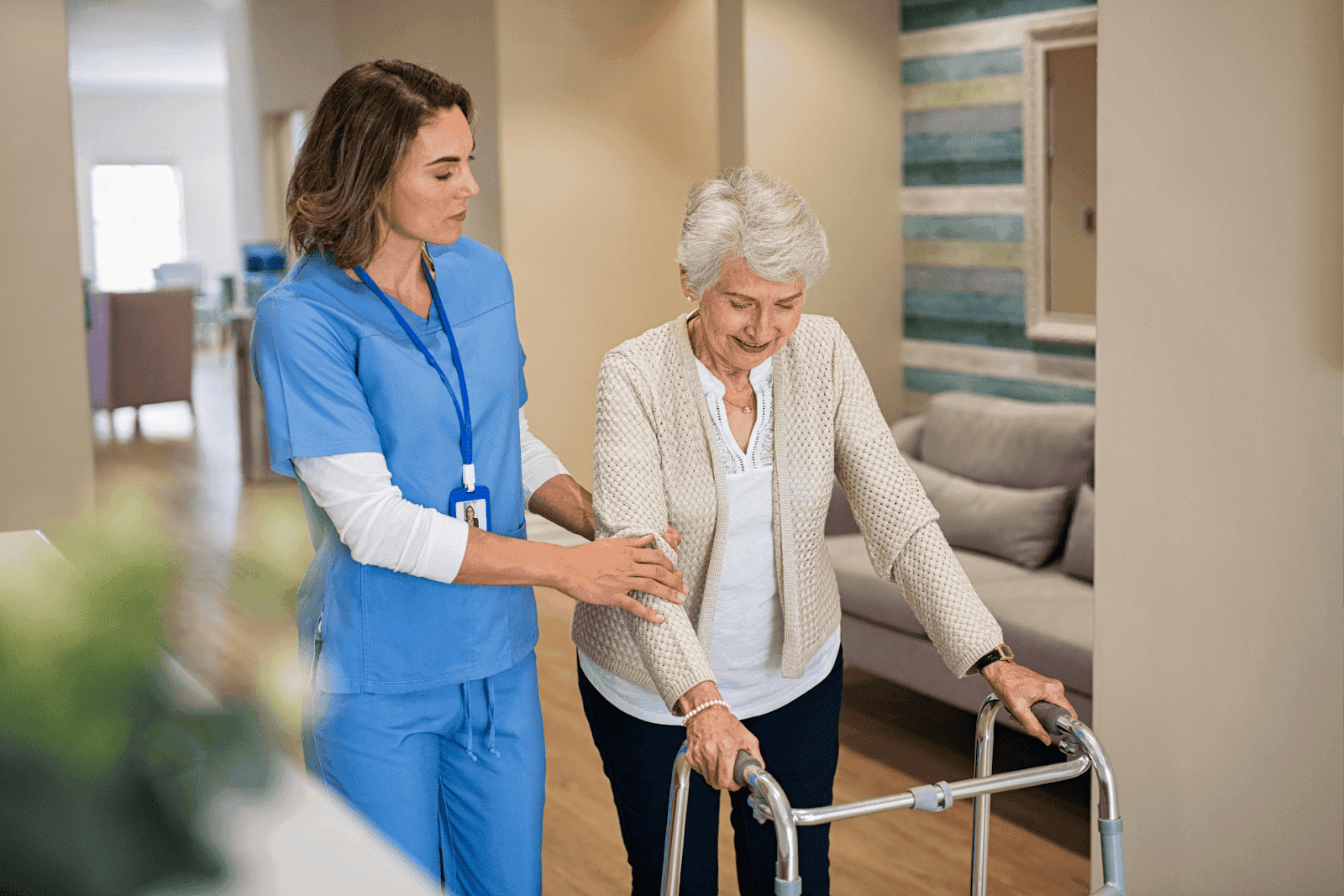A nurse assists an elderly woman using a walker