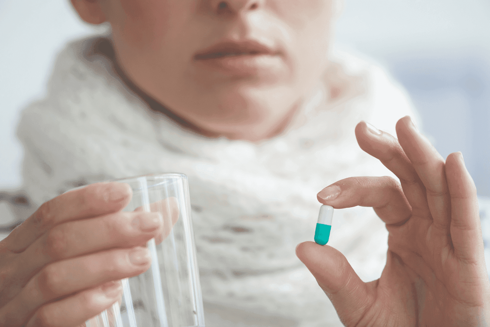 A person holding a glass of water in one hand and a two-toned capsule in the other, preparing to take medication.