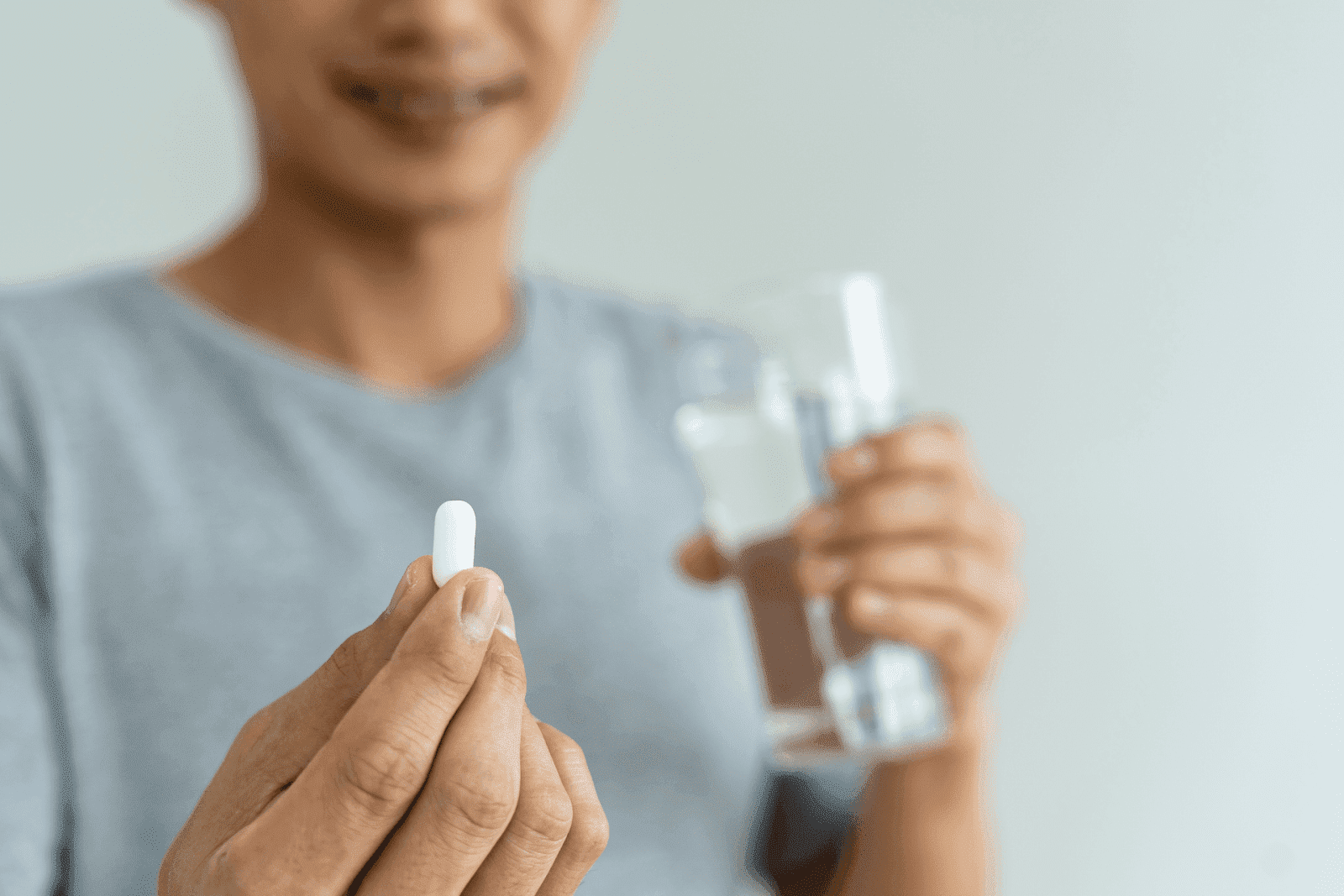 A person holding a white pill in one hand and a glass of water in the other.