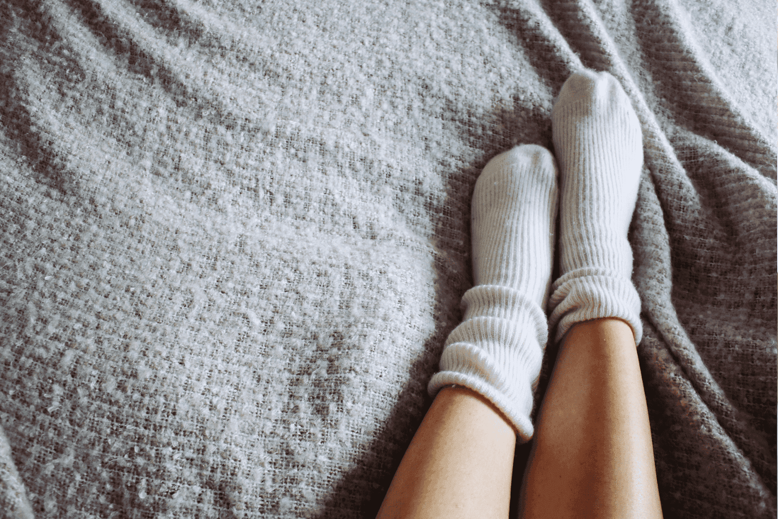 A person is lying down on a cozy bed, wearing warm white socks