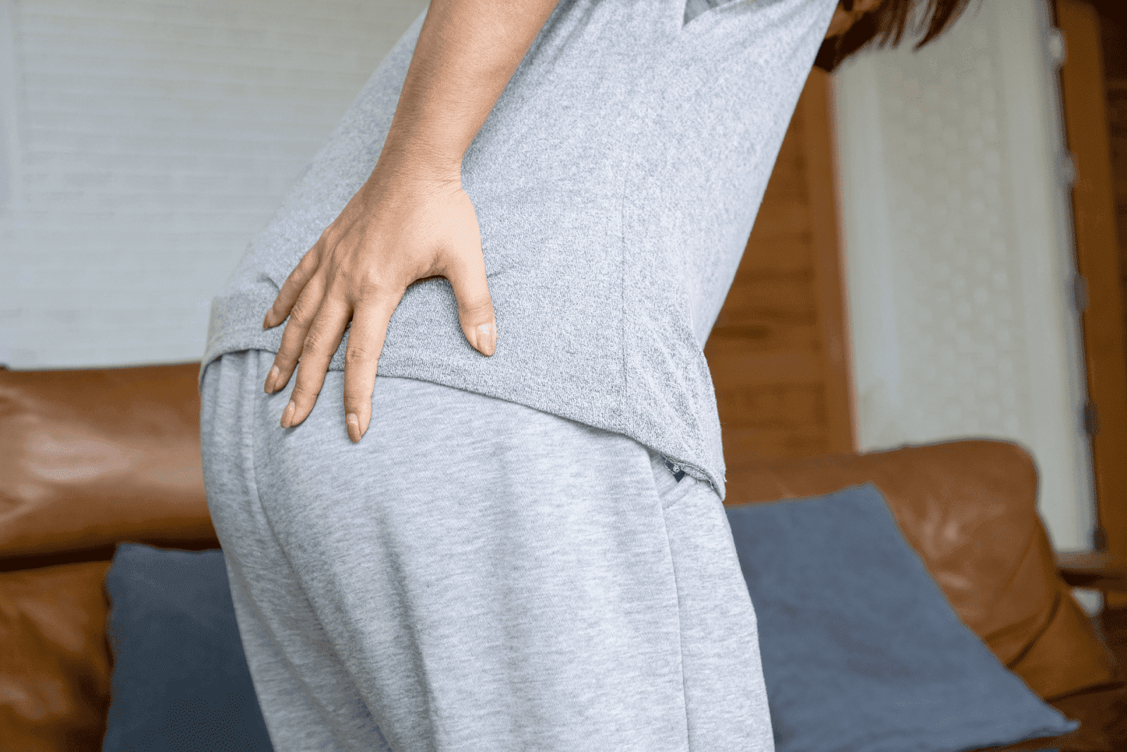 A person is shown holding their lower back/hip area, with a posture that suggests discomfort or pain