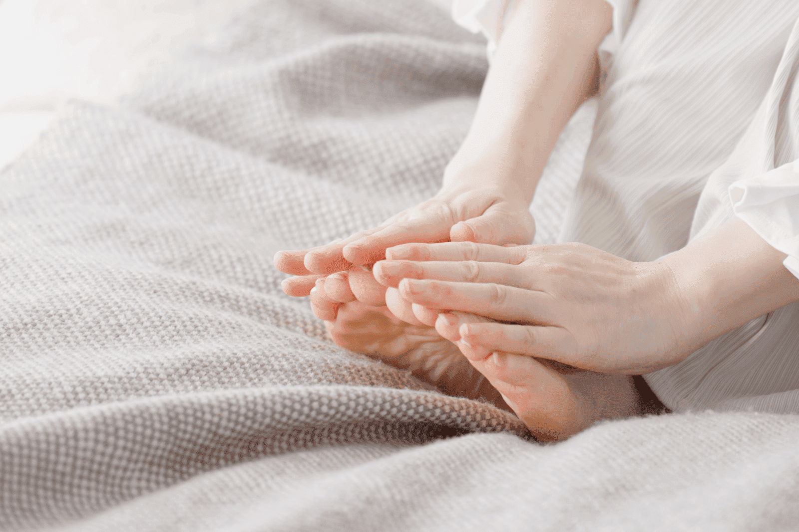 A person is sitting on a soft blanket, gently holding or massaging their bare feet with both hands