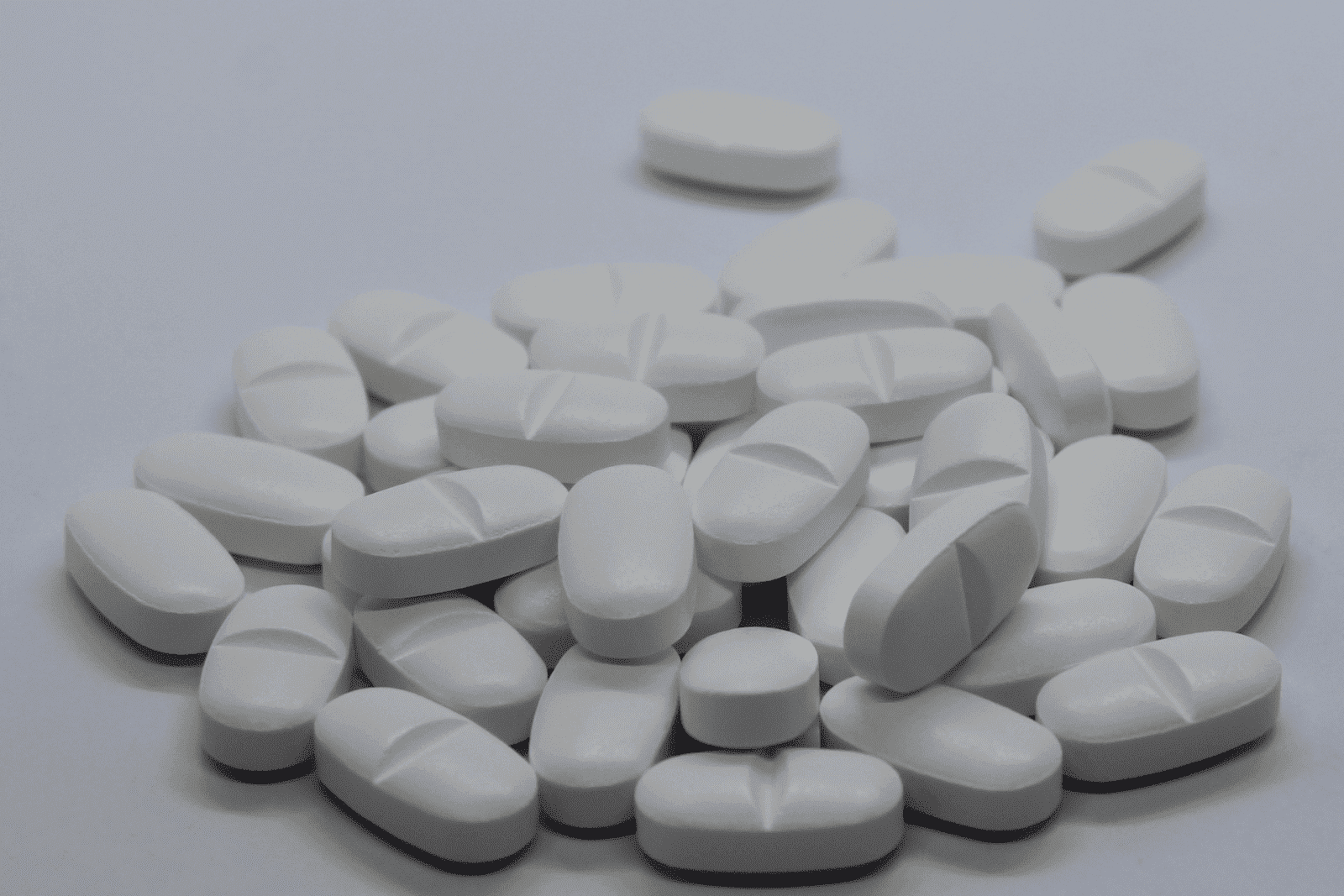 A pile of white oval tablets scattered on a plain surface