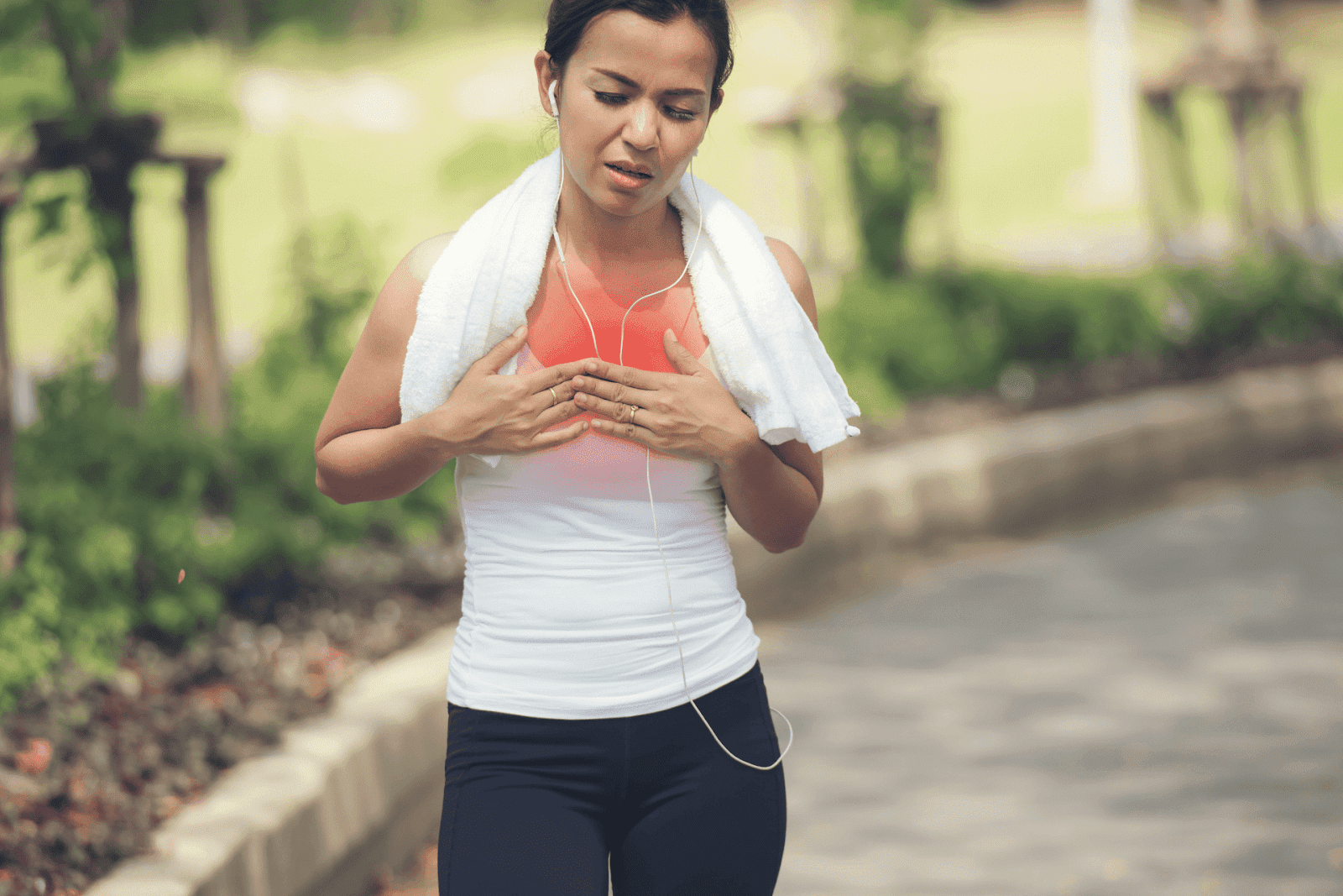 A woman clutches her chest in pain while jogging outdoors, showing signs of chest discomfort