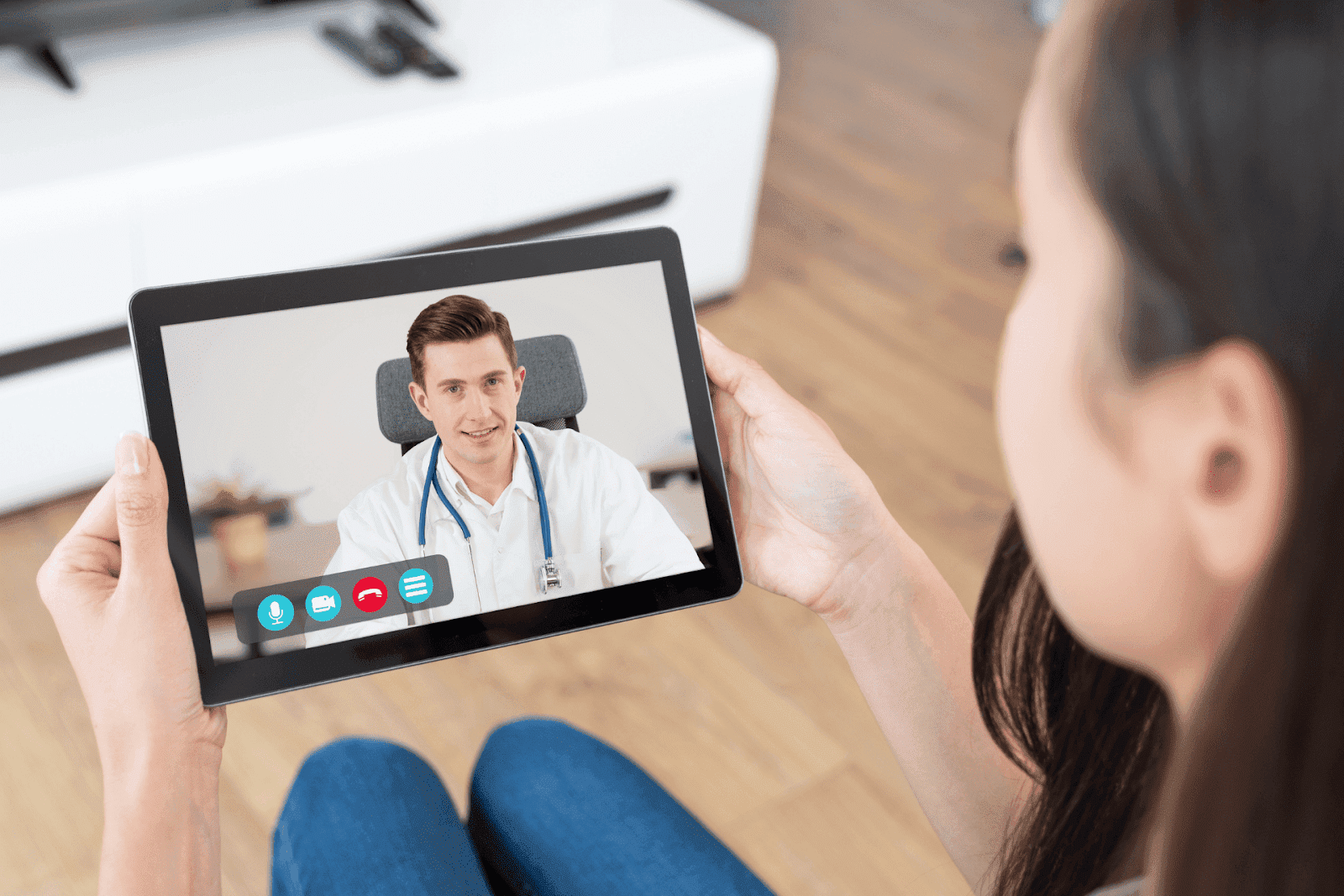 A woman holds a tablet showing a male doctor during a virtual consultation