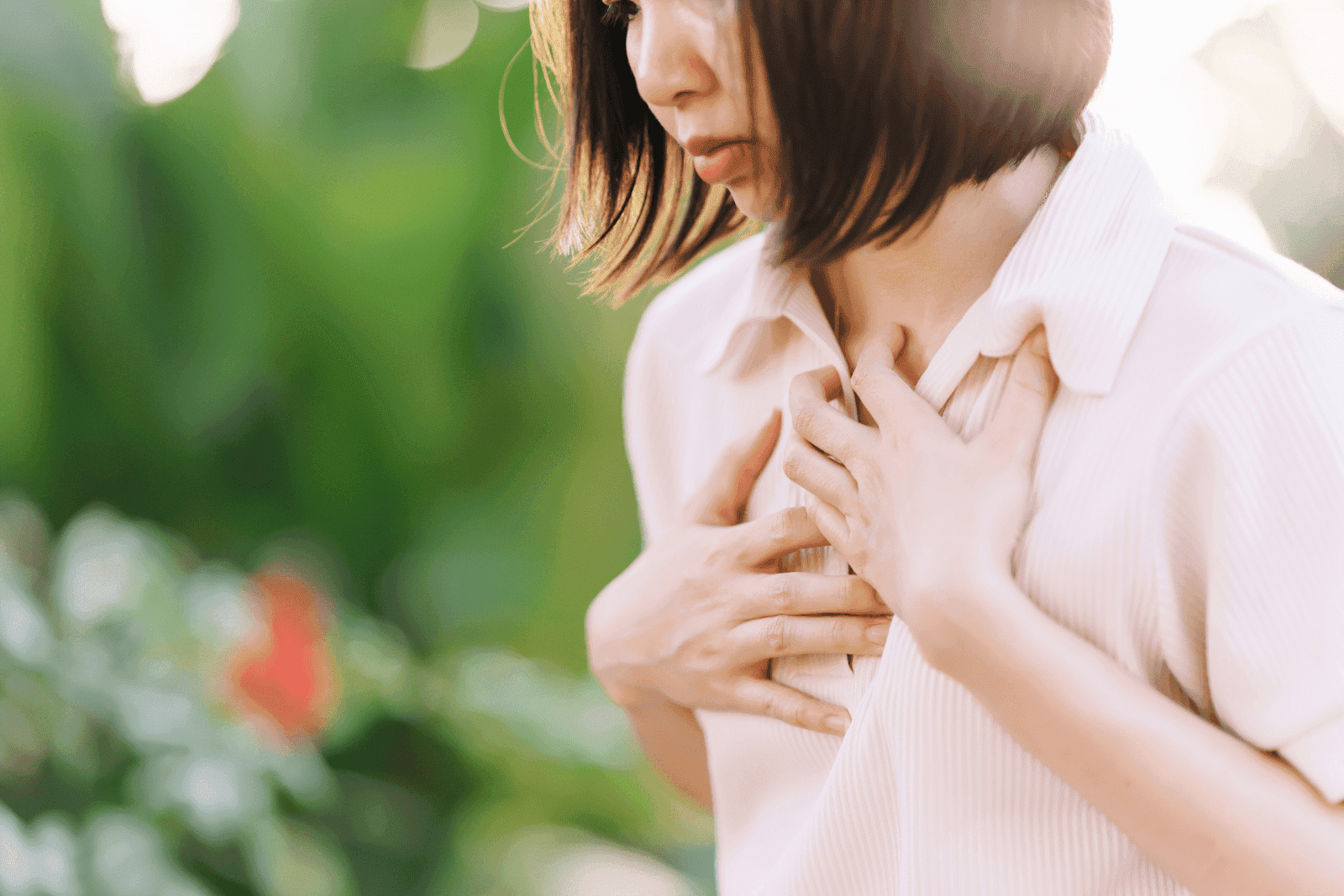 A woman holds her chest outdoors, appearing to experience chest discomfort or shortness of breath