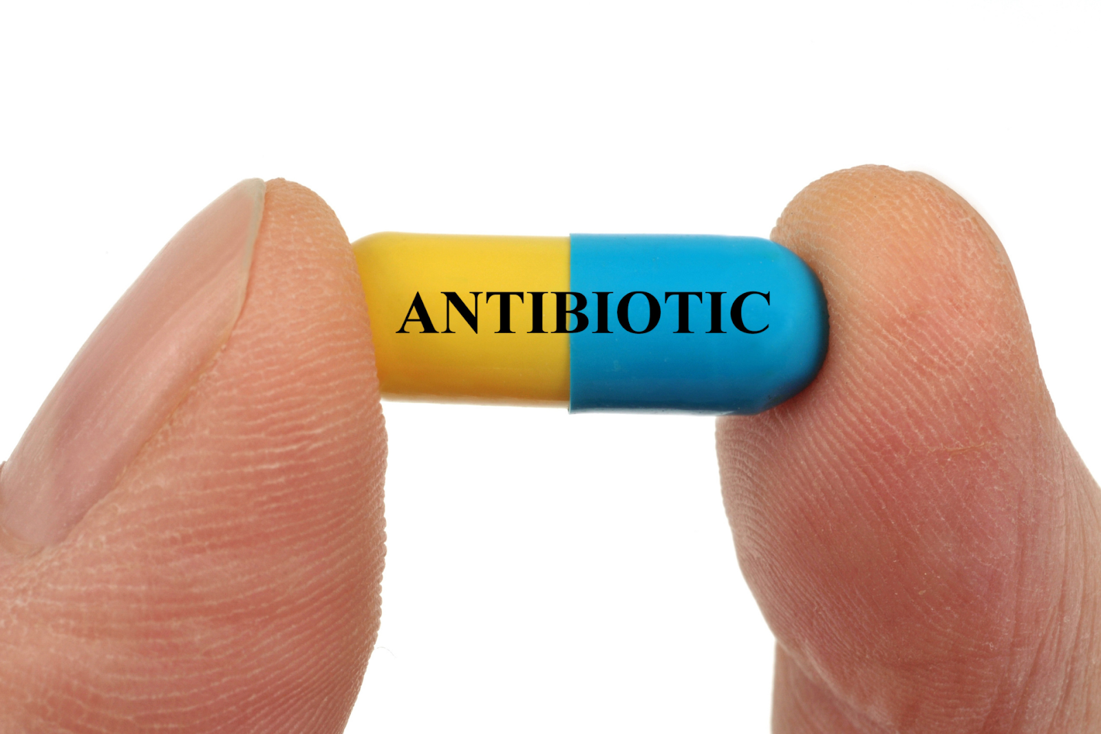 A yellow-and-blue capsule held between two fingers with the word ‘Antibiotic’ printed on it.