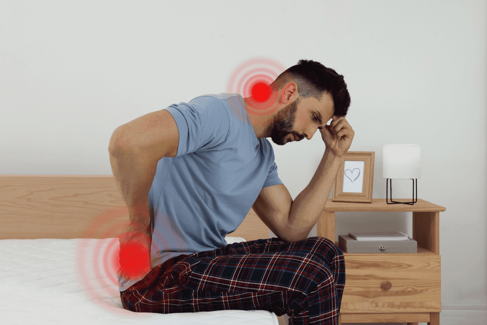 A younger man sits on the edge of a bed, leaning forward in pain.