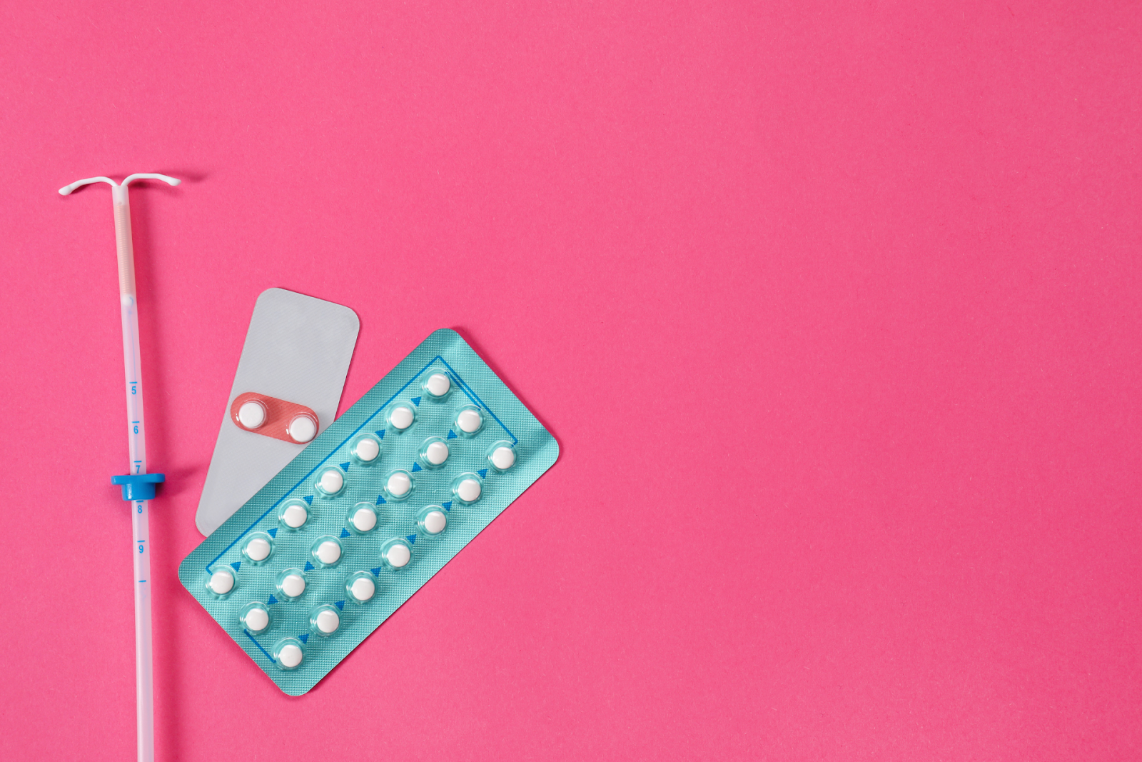 An intrauterine device (IUD) and blister packs of birth-control pills on a pink background.