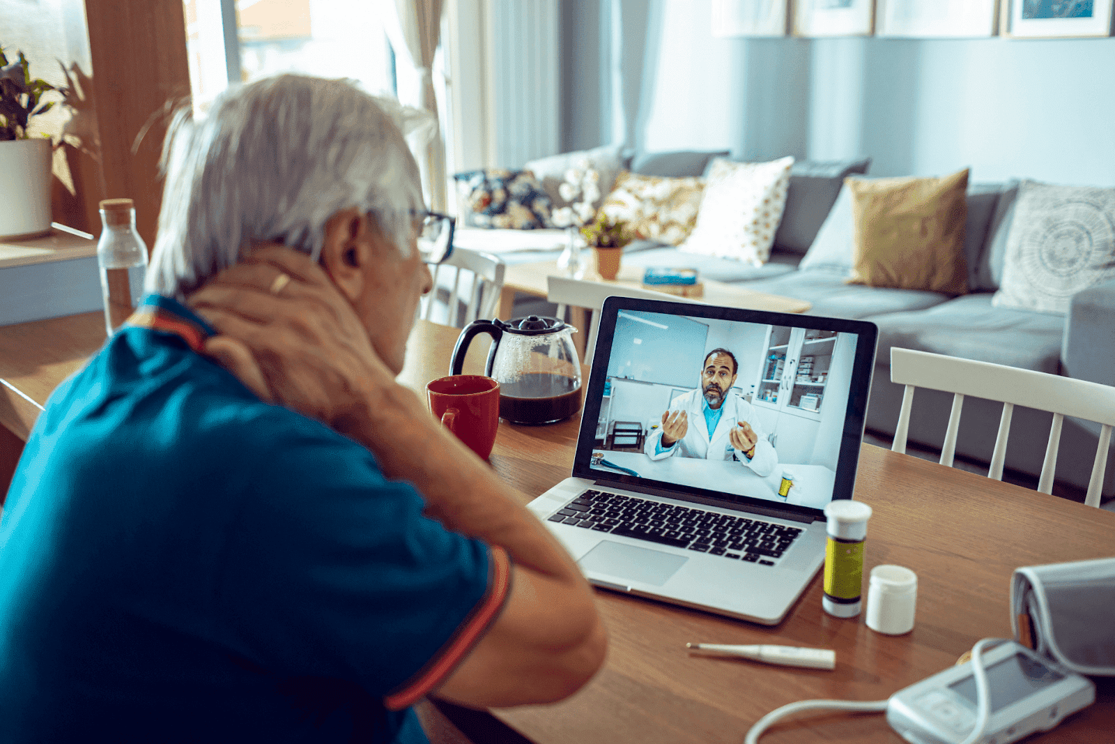 An older man holding his neck due to pain is having a telemedicine consultation at home.