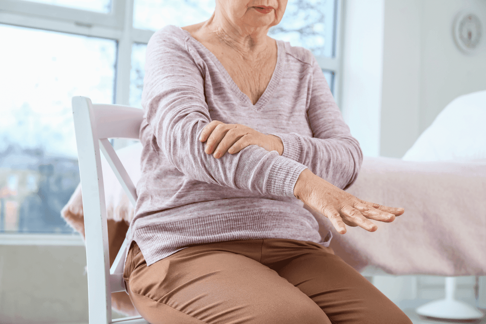 An older woman sits on a chair, experiencing shakiness in her arm