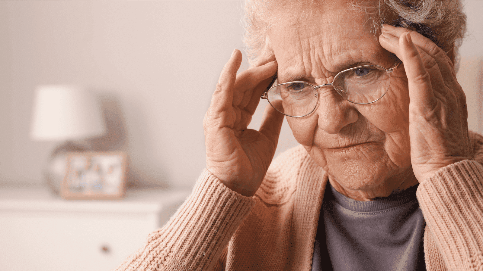 An older woman with glasses holds her temples, looking distressed, due to a memory loss