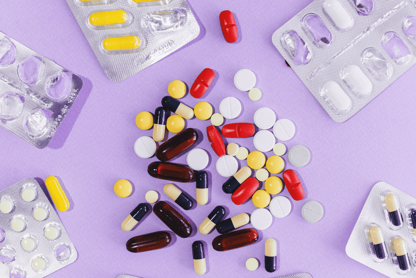 Assorted colorful pills and capsules spread out on a purple surface with blister packs around them