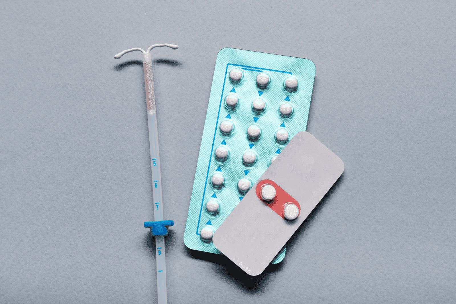 Birth control pills and an IUD on a gray background.