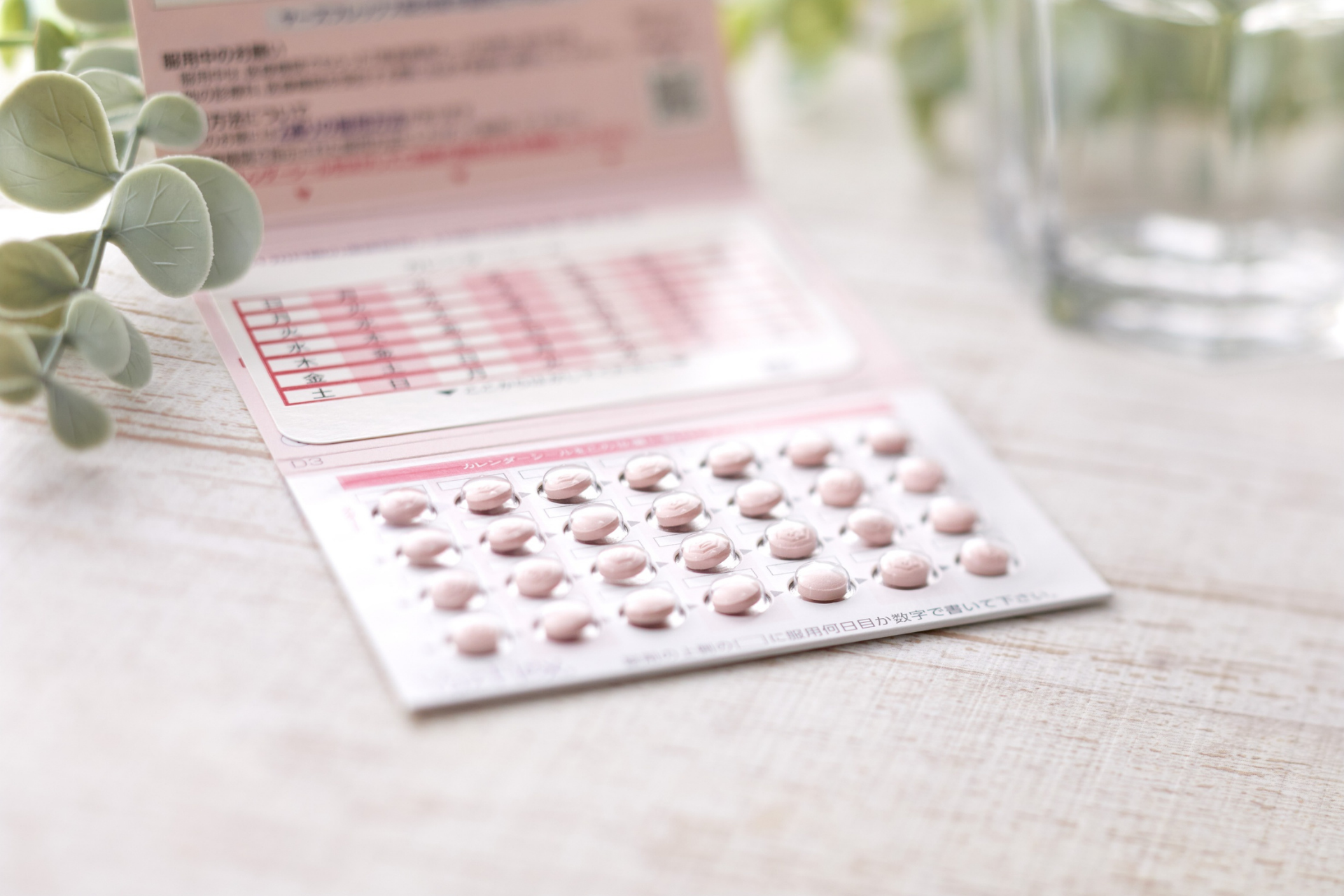 Blister pack of pink oral contraceptive pills on a light wooden table