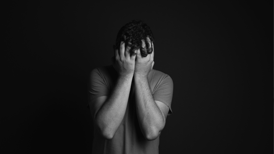 Black and white image with a man covering his face with his hands.