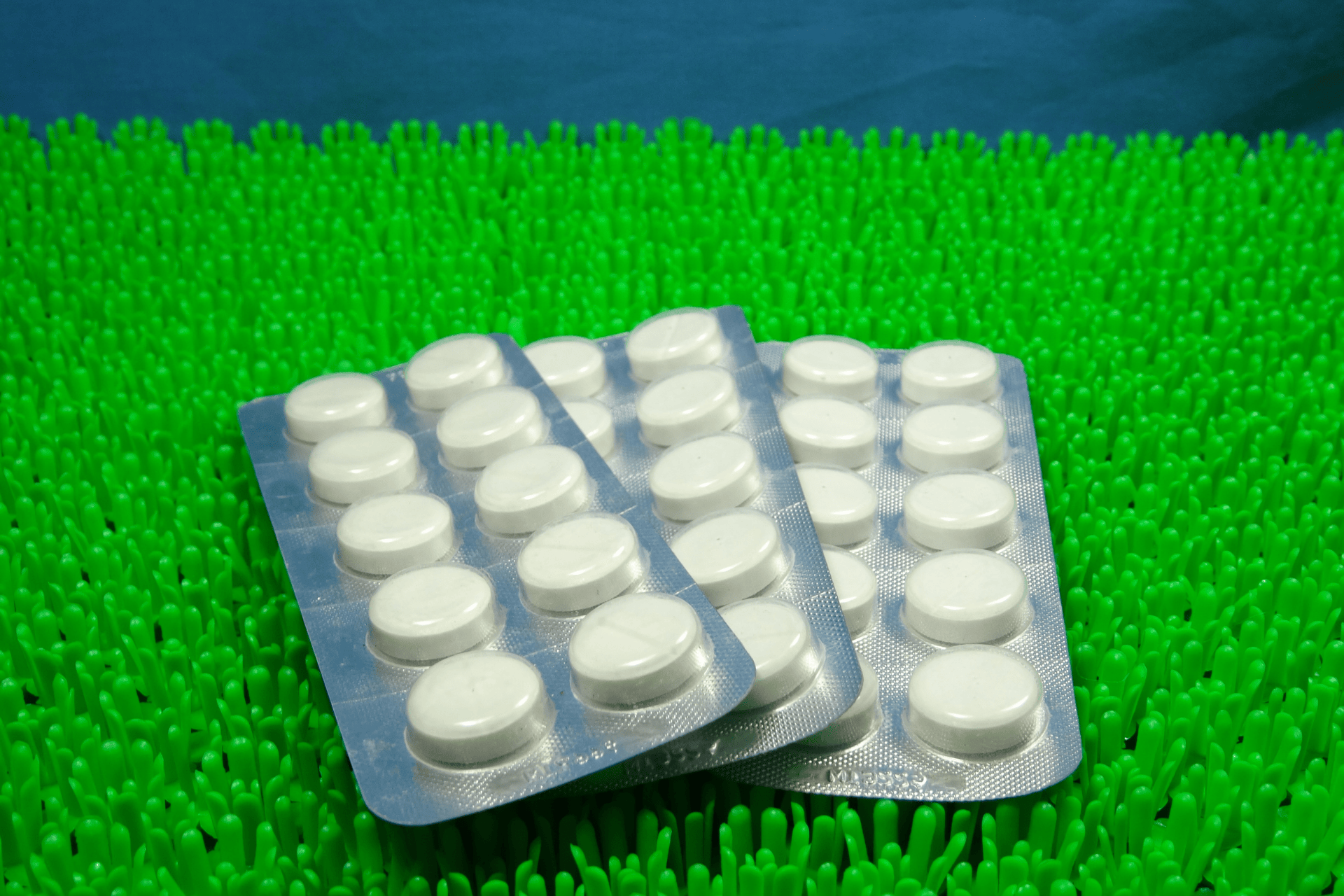 Blister packs of white tablets placed on a bright green textured surface.