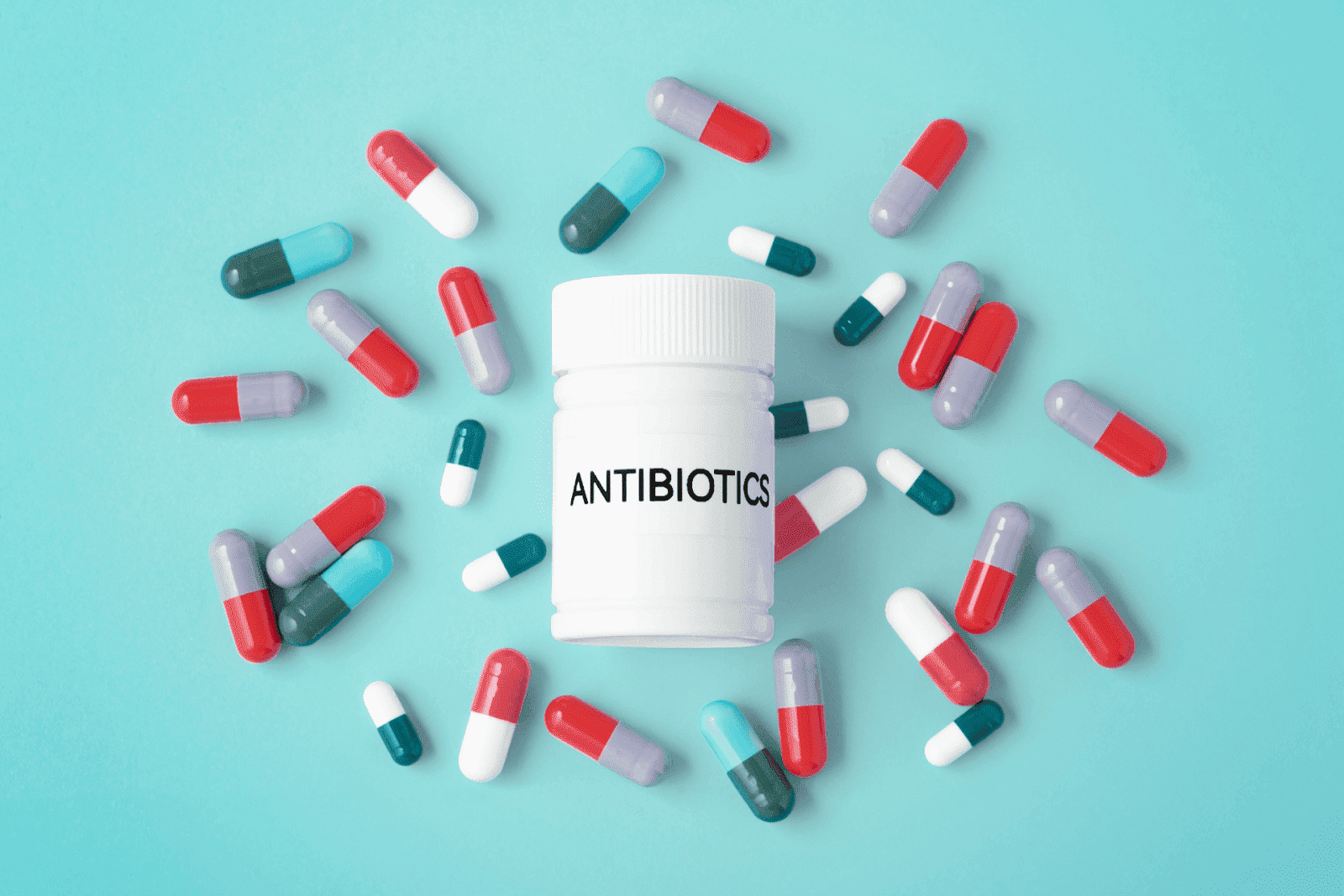 Bottle labeled “Antibiotics” surrounded by assorted colorful capsules on a blue background