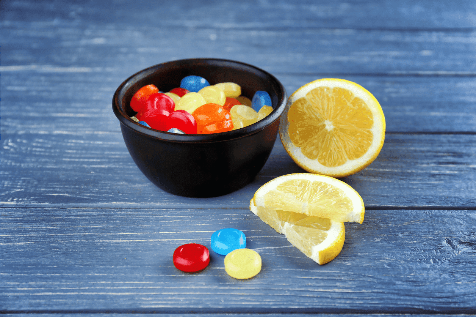 Bowl of colorful lozenges with sliced lemons on a wooden table.