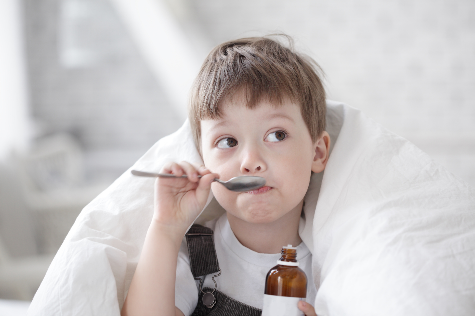 Child holding a spoon and medicine bottle while wrapped in a blanket