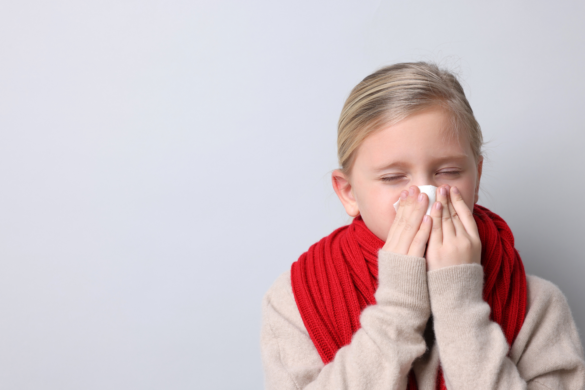 Child wearing a red scarf and holding a tissue to their nose, appearing sick