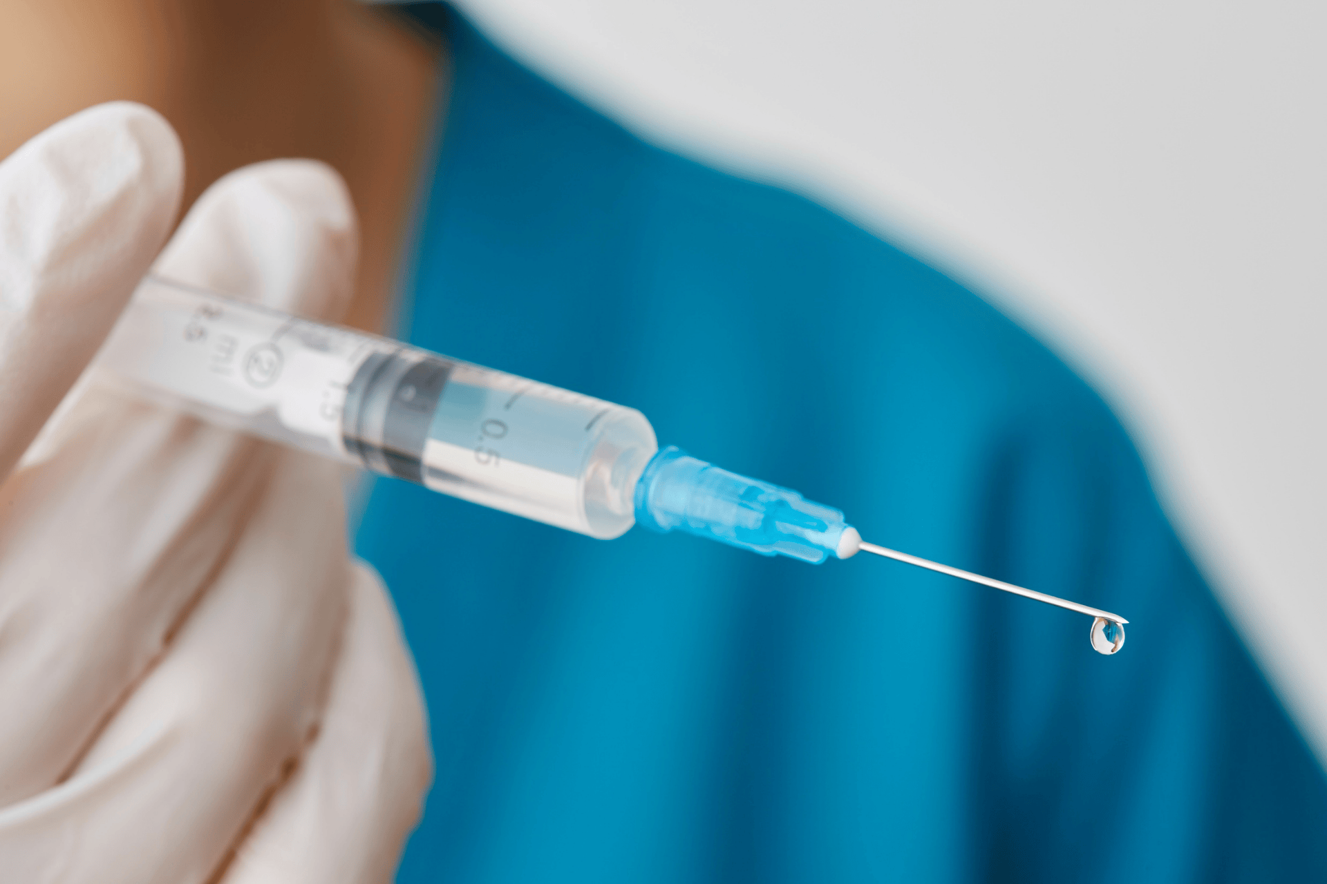 close-up of a gloved hand holding a syringe with a droplet on the needle tip