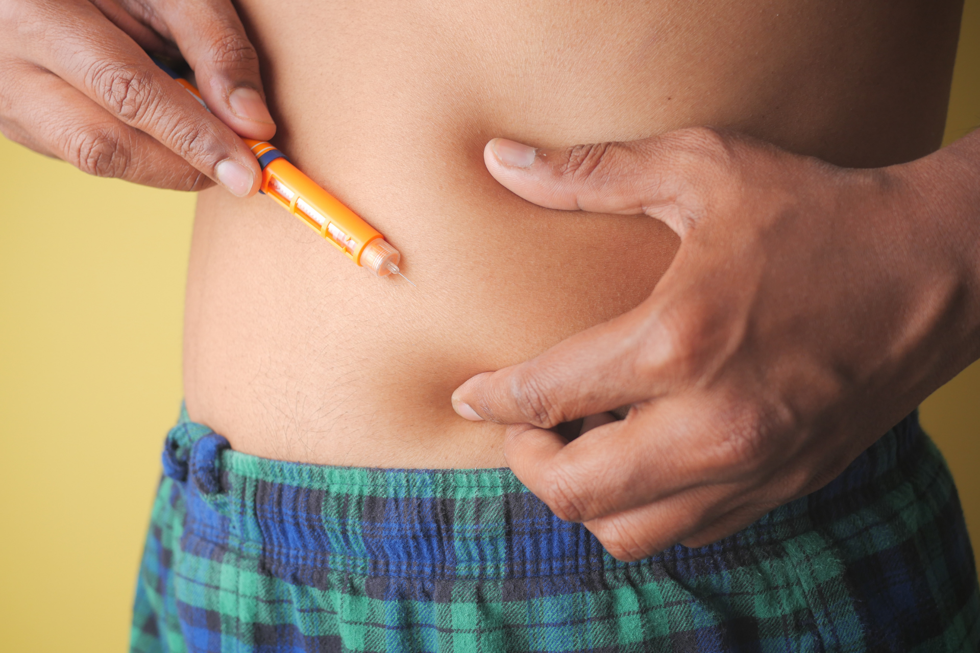 Close-up of a person injecting their abdomen with an orange insulin pen.