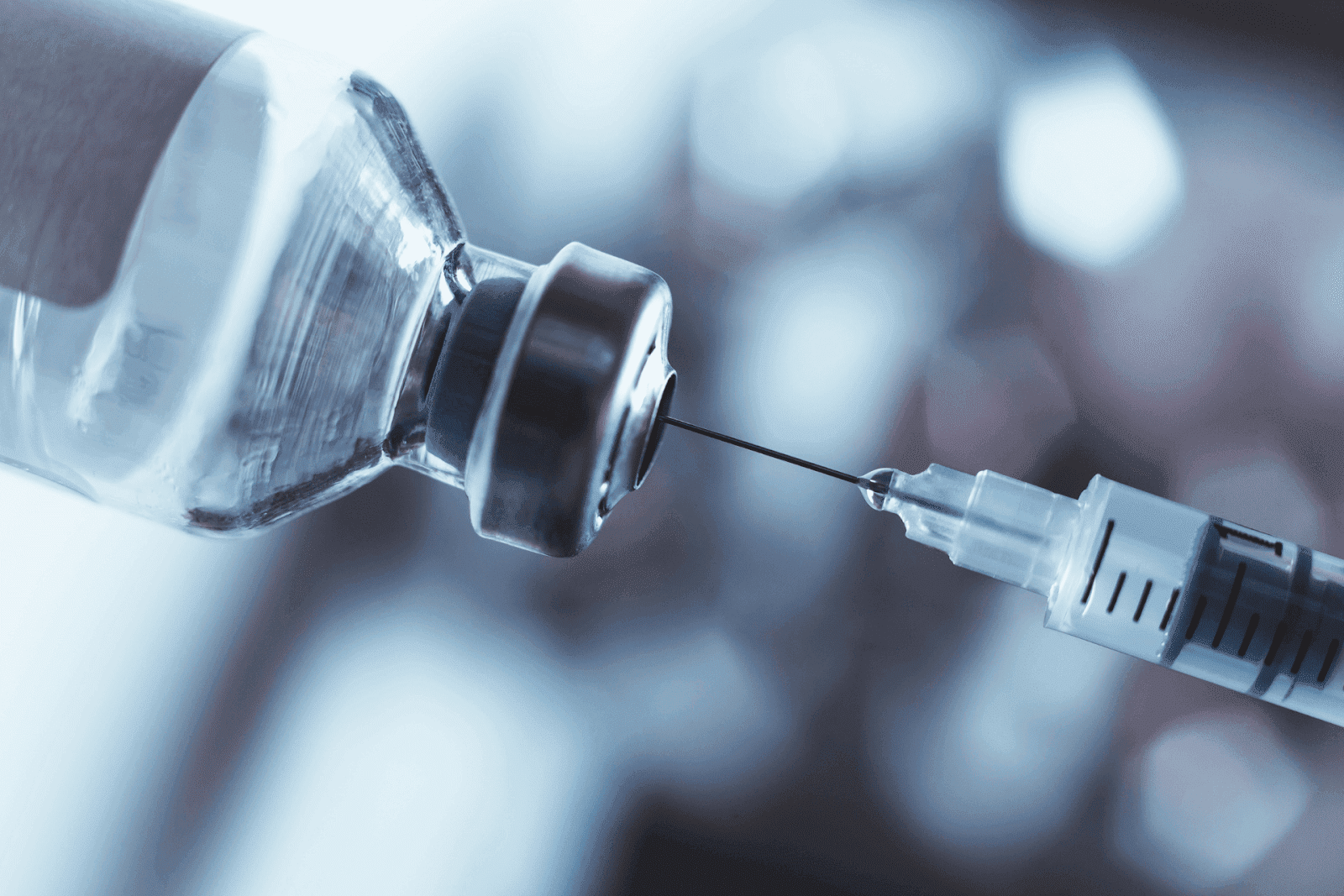 Close-up of a syringe drawing liquid from a vial with a blurred background.