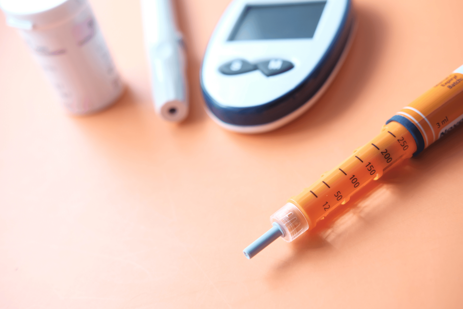 Close-up of an orange insulin pen with a glucose meter and supplies on a table.