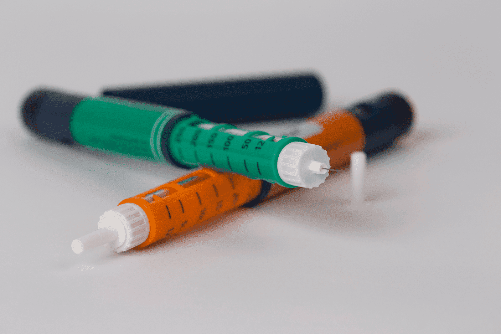 Close-up of colorful insulin pens with needles on a white surface.