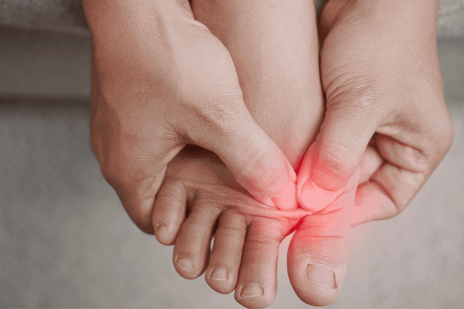 Close-up of hands pressing on the inflamed area between toes, indicating foot pain.