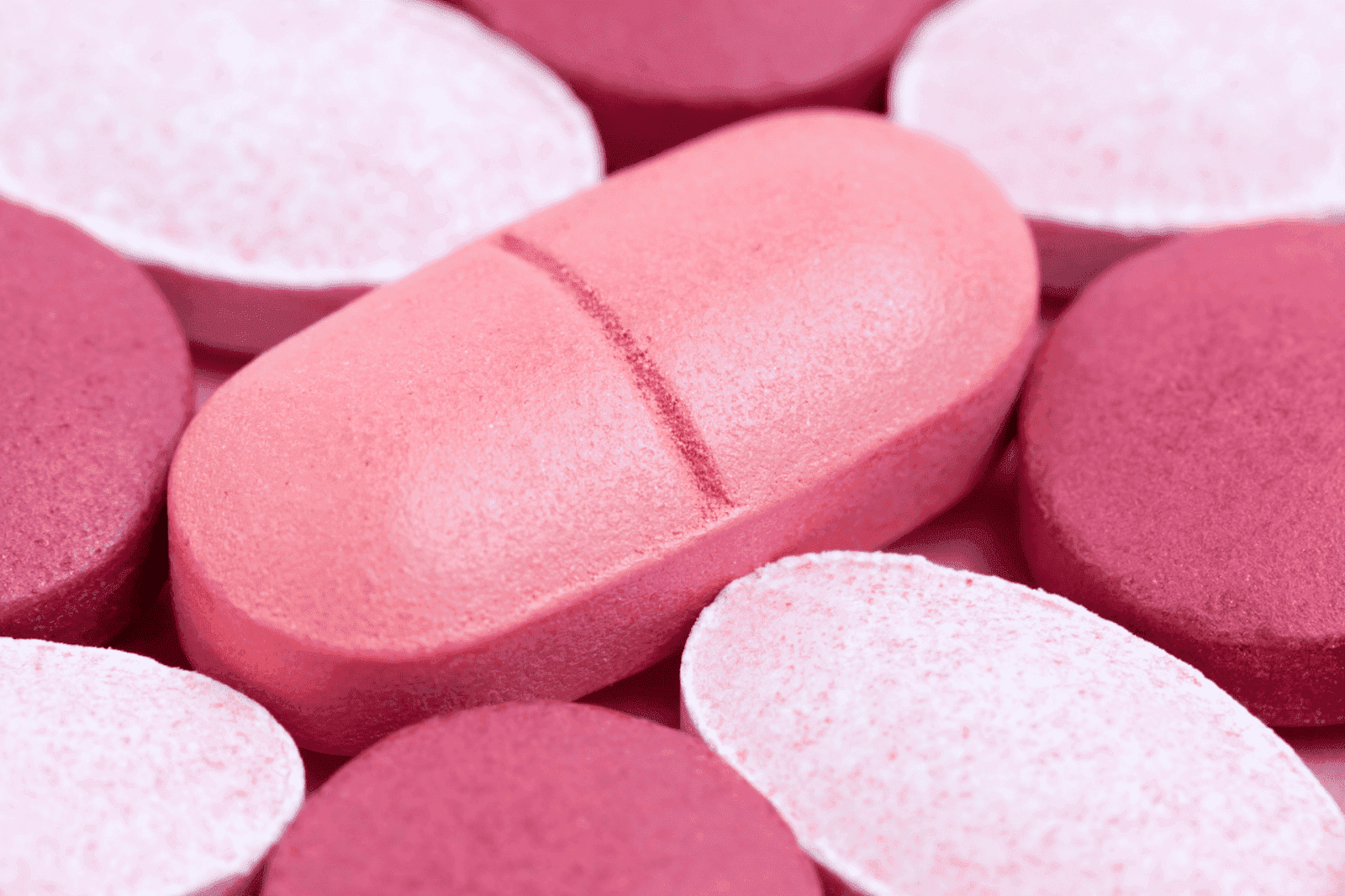 Close-up of pink and white tablets, with one large pink pill in focus.
