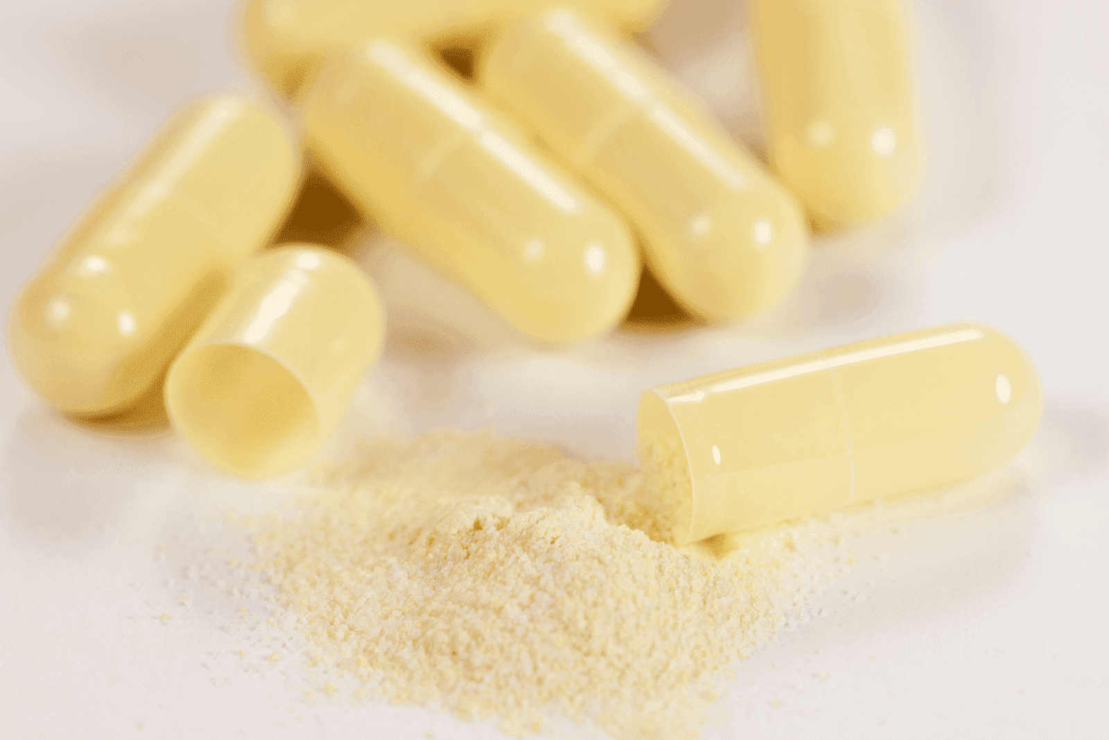 Close-up of yellow capsules, one opened with powder spilled on a white surface.