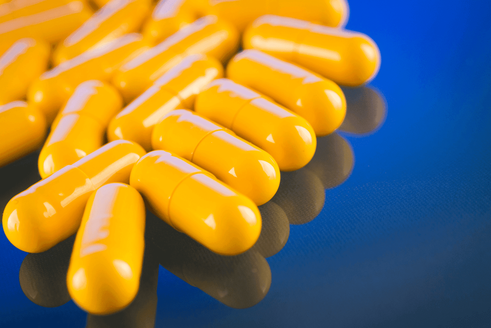 Close-up of yellow capsules on a reflective blue surface.