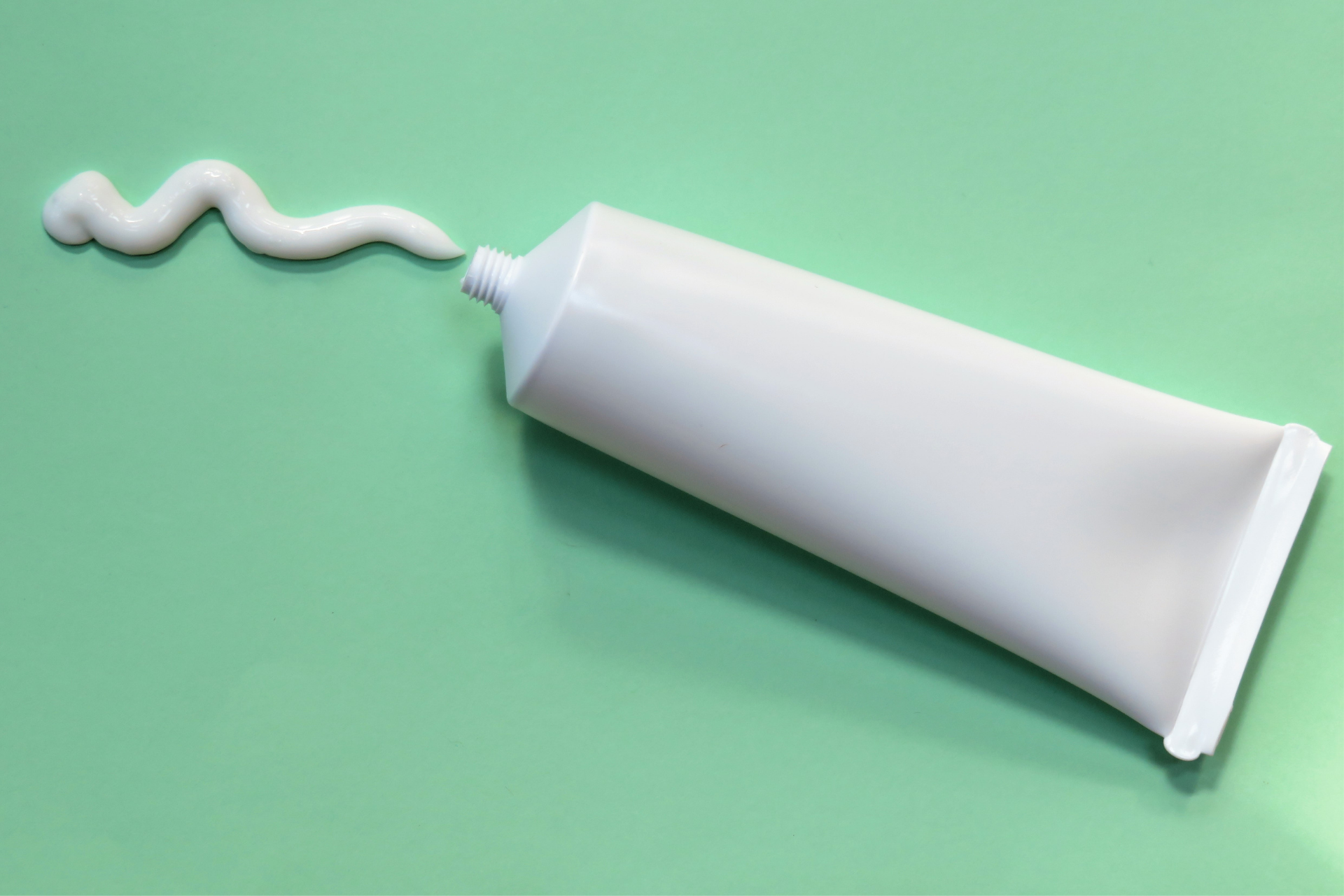 A white squeeze tube with cream coming out onto a green surface