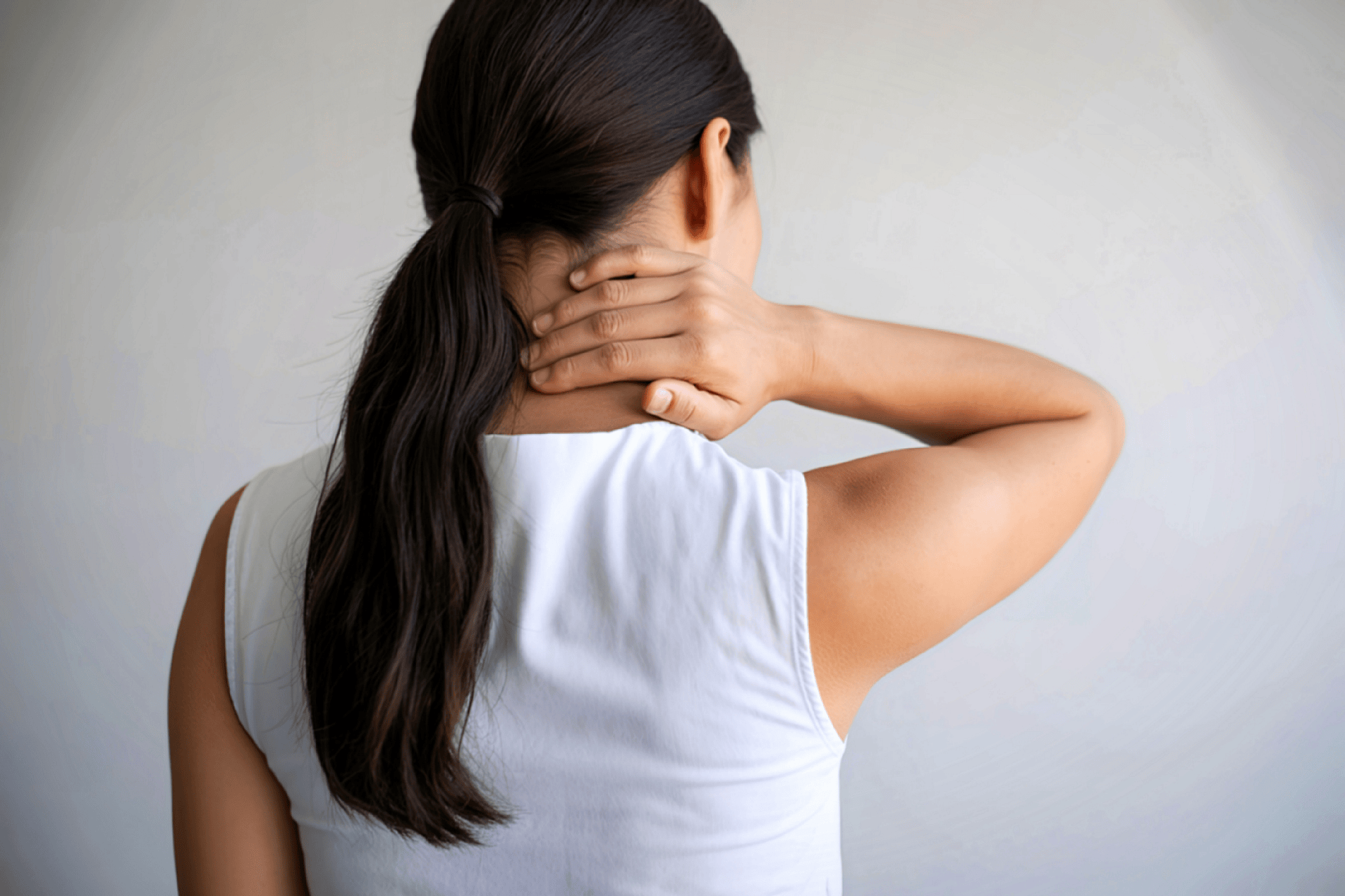A woman seen from behind holds the back of her neck, suggesting neck pain or stiffness associated with cervical arthritis.