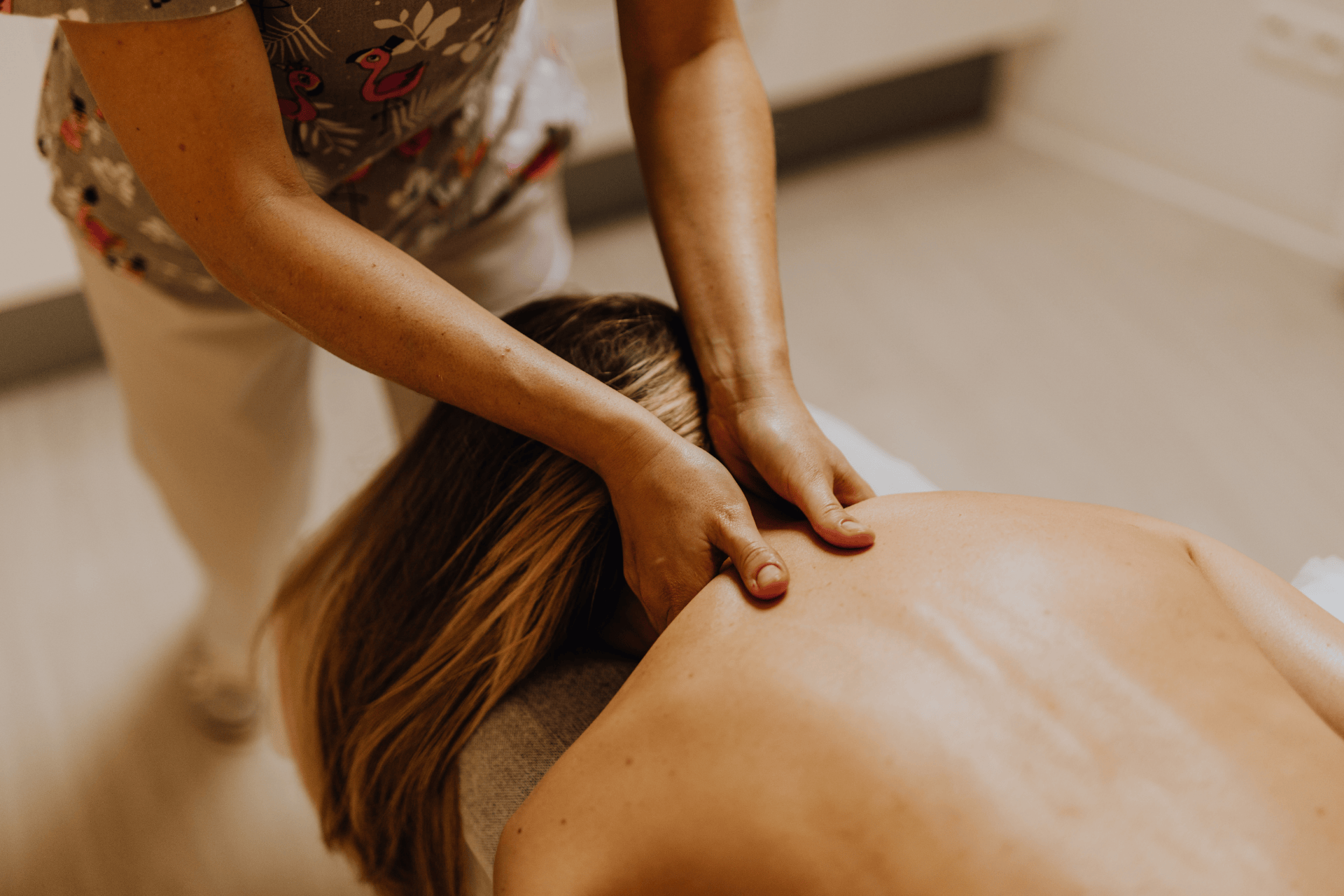 Massage therapist applying pressure to a woman’s upper back and shoulders during a treatment session.