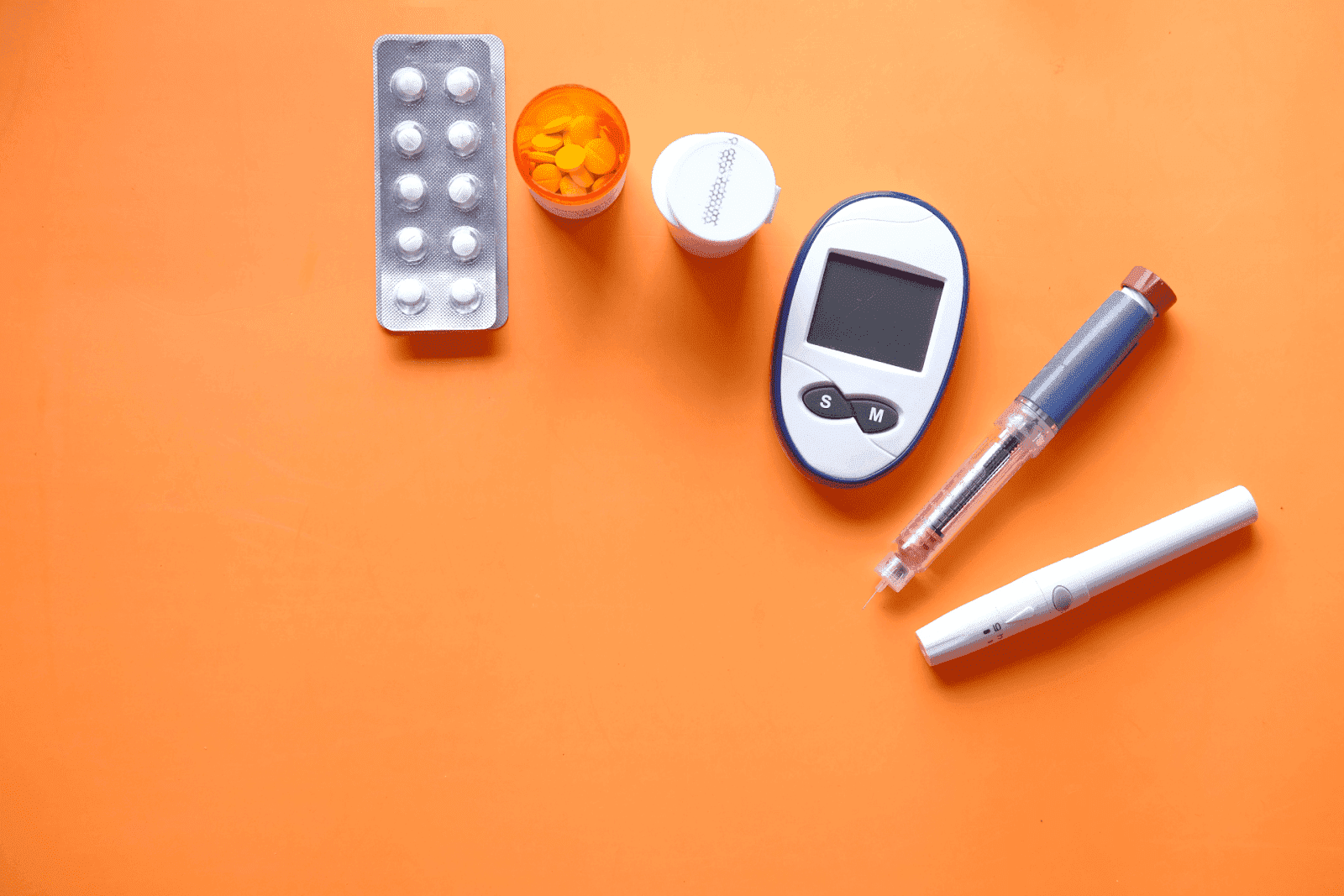 Diabetes management tools with pills, glucometer, and insulin pen on orange background.