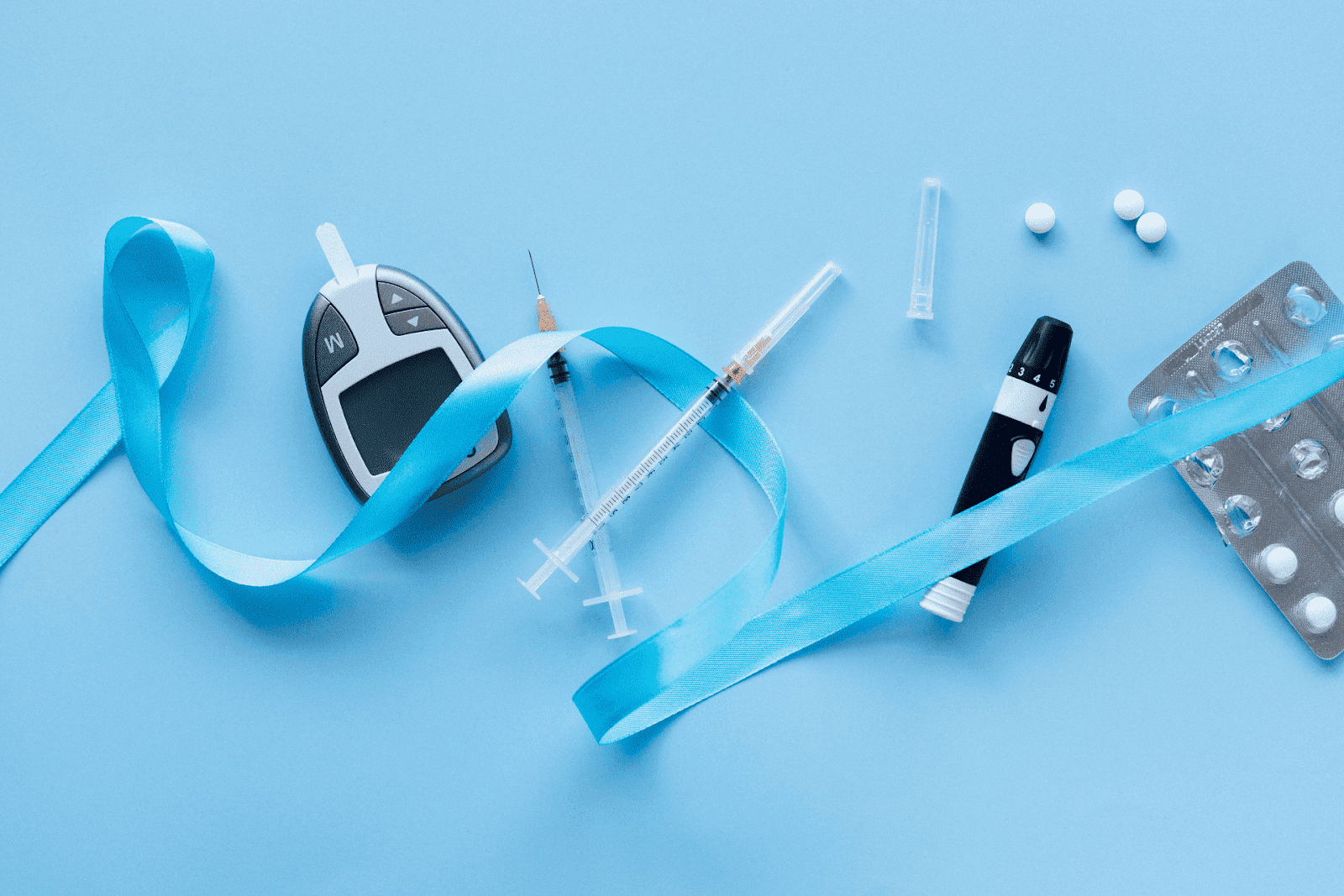 Diabetes supplies including glucometer, syringes, pills, and blue ribbon on light blue background