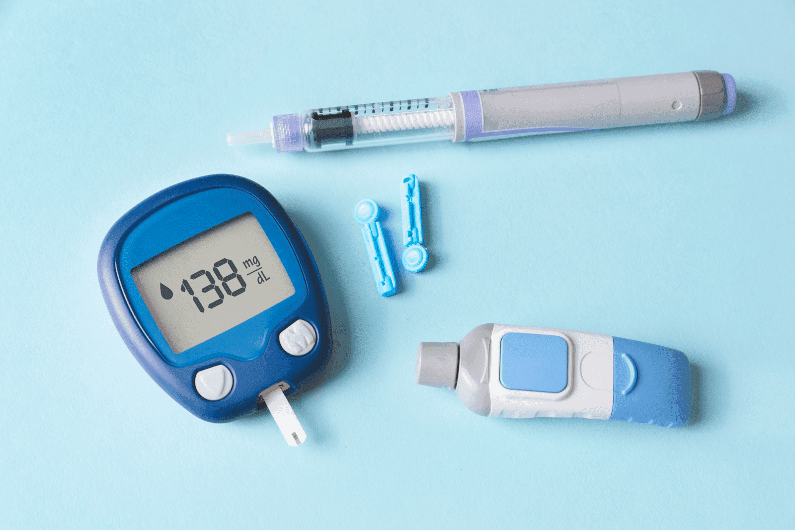 Diabetes supplies on a blue background: a glucose meter reading 138 mg/dL, an insulin pen, and lancets.