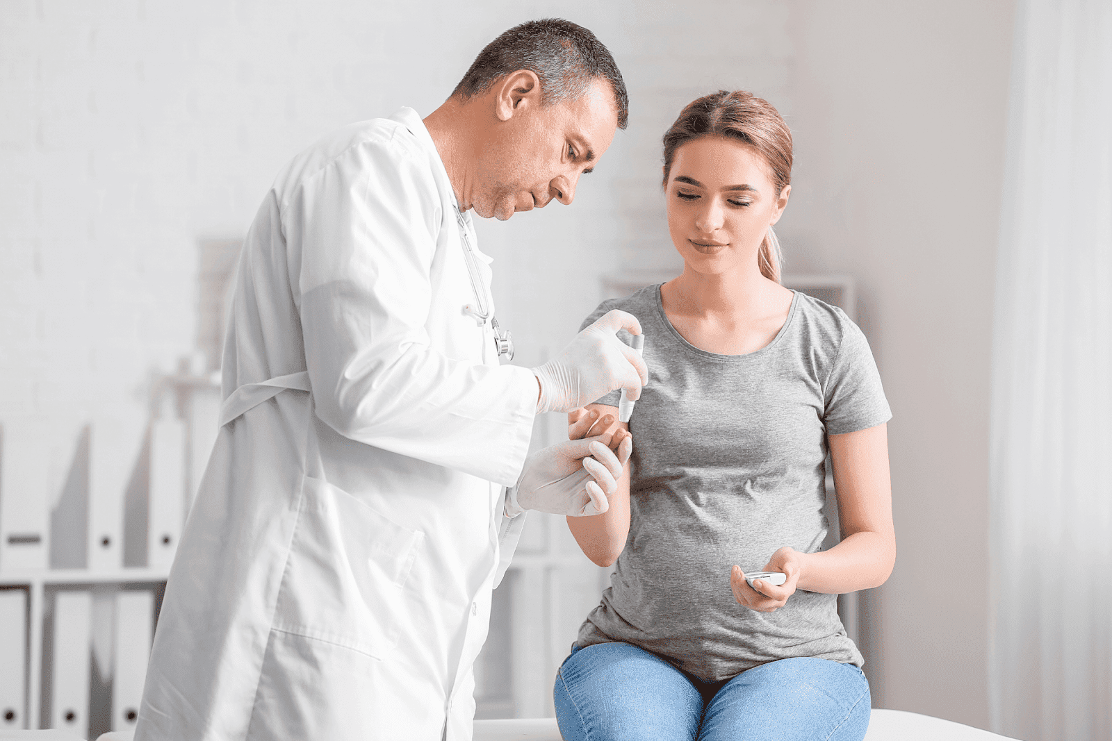 Doctor assisting a pregnant woman with checking her blood sugar using a glucose meter.
