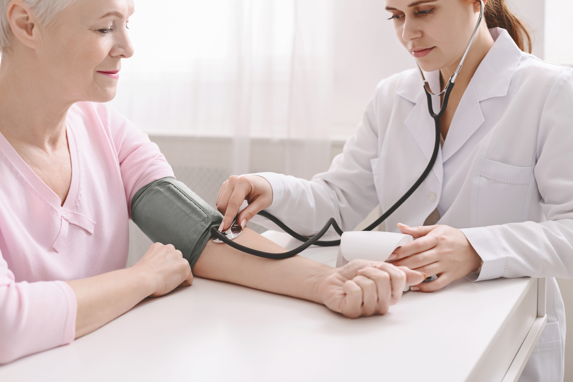 Doctor checking an older woman’s blood pressure with a cuff and stethoscope at a clinic
