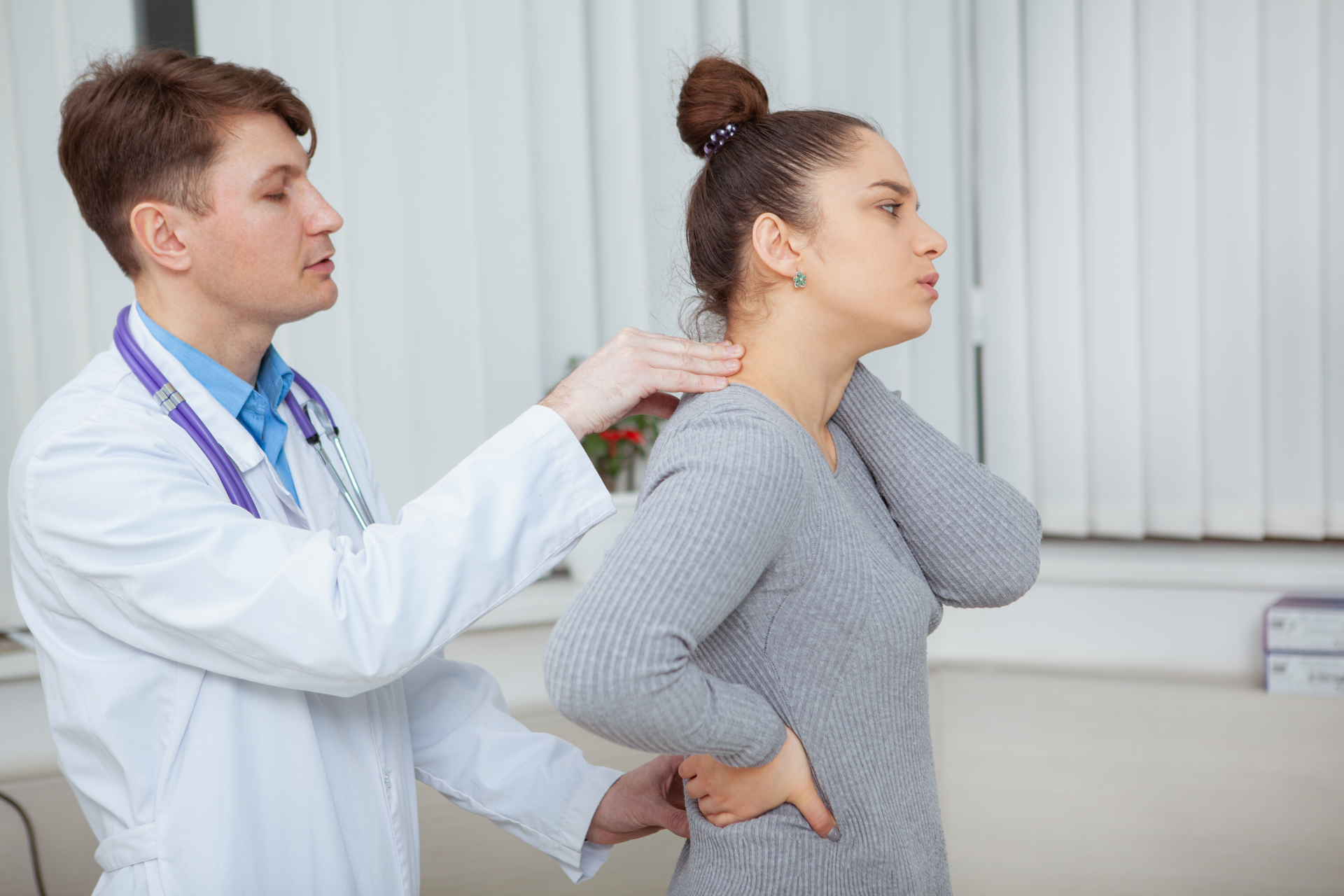 Doctor examining a woman’s neck and upper back during a clinical checkup