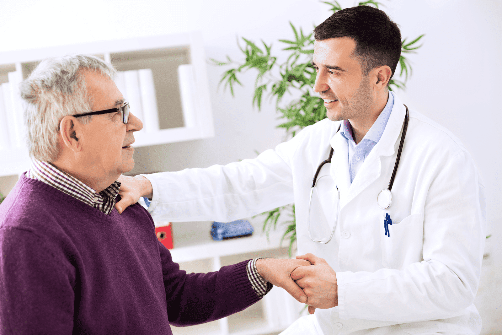 Doctor greeting an older male patient with a handshake and smile during consultation
